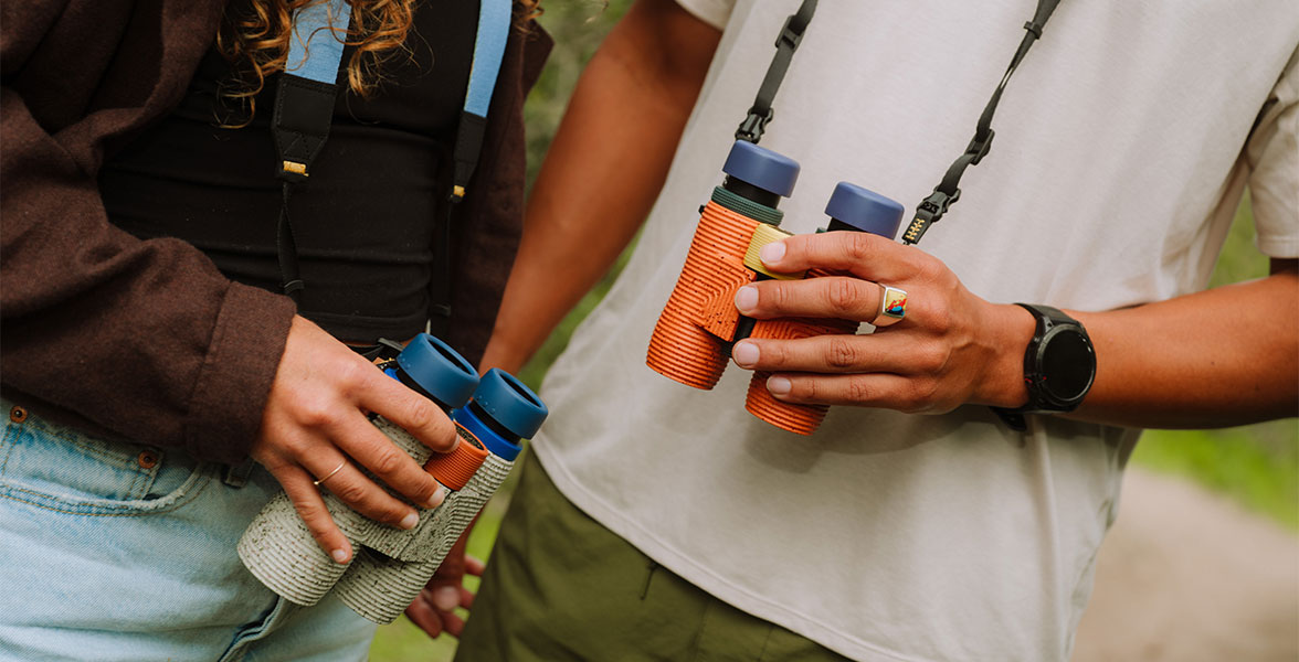 Two people standing next to each other hold binoculars.