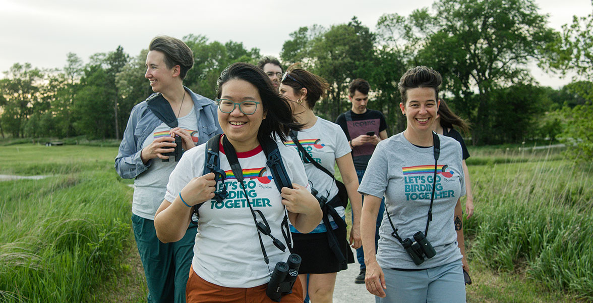 People on a bird walk donned with binoculars and Let's Go Birding Together apparel.
