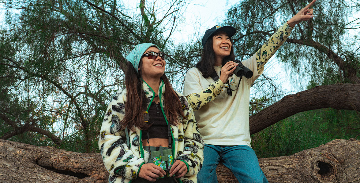 Two people with binoculars on a bird outing. The person on the right points to something on the right.