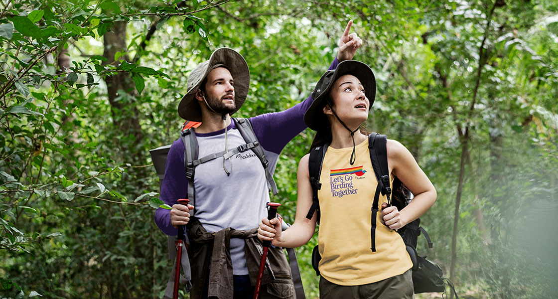 Two people on a bird outing. The person to the left points to something on the right. The other person looks that direction.
