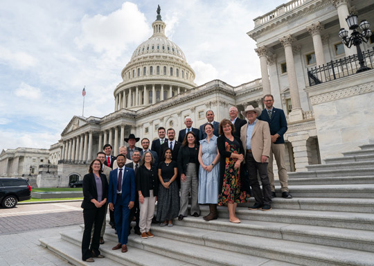 Photo of a group of people standing on the steps of the US Capitol. 